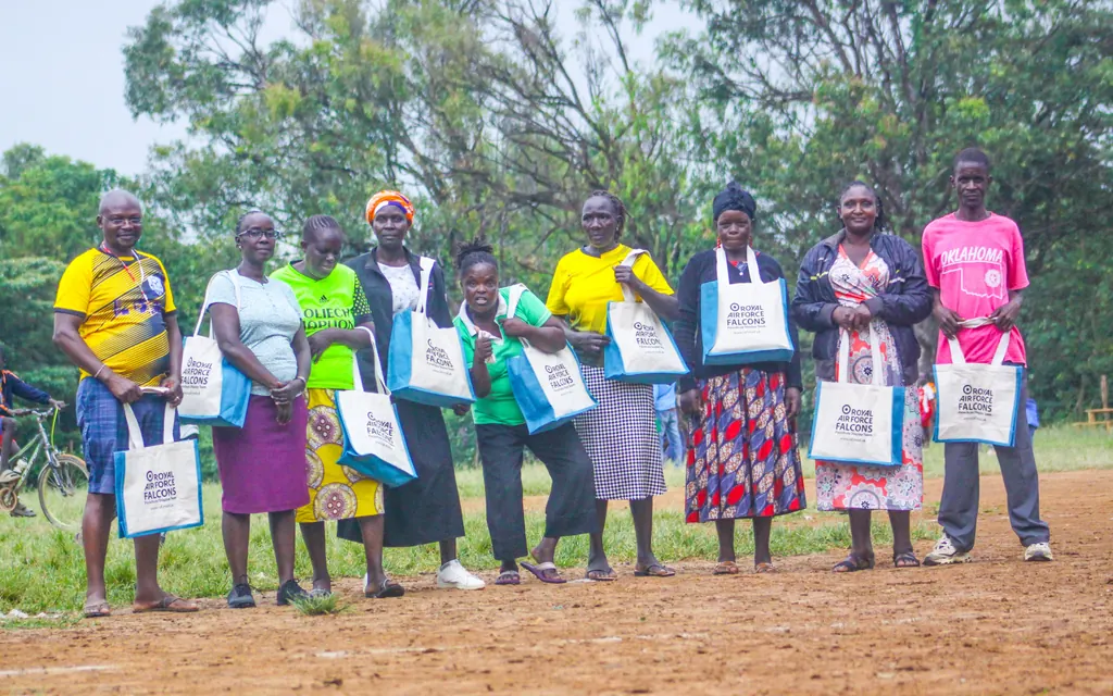 Nine community members standing together beside the pitch, each holding a matching tote bag.