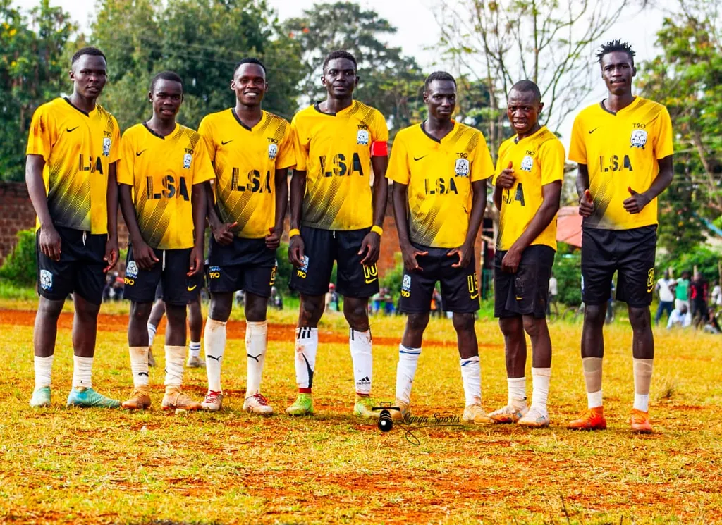 Seven Ligega Sports players in yellow LSA shirts and black shorts standing together on the pitch.
