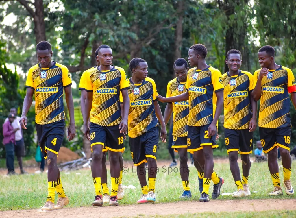 Ligega Sports players in yellow and black Mozzart kit walking together across the pitch during a match.