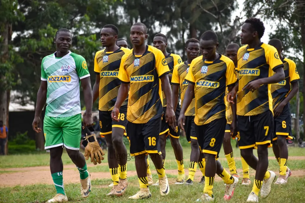 The Ligega Sports team in yellow and black Mozzart kit walking onto the pitch, led by their goalkeeper in green.