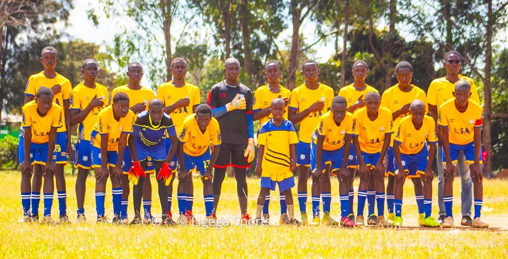The Ligega Sports under-15 squad in yellow and blue kit, lined up in two rows in front of a school building.