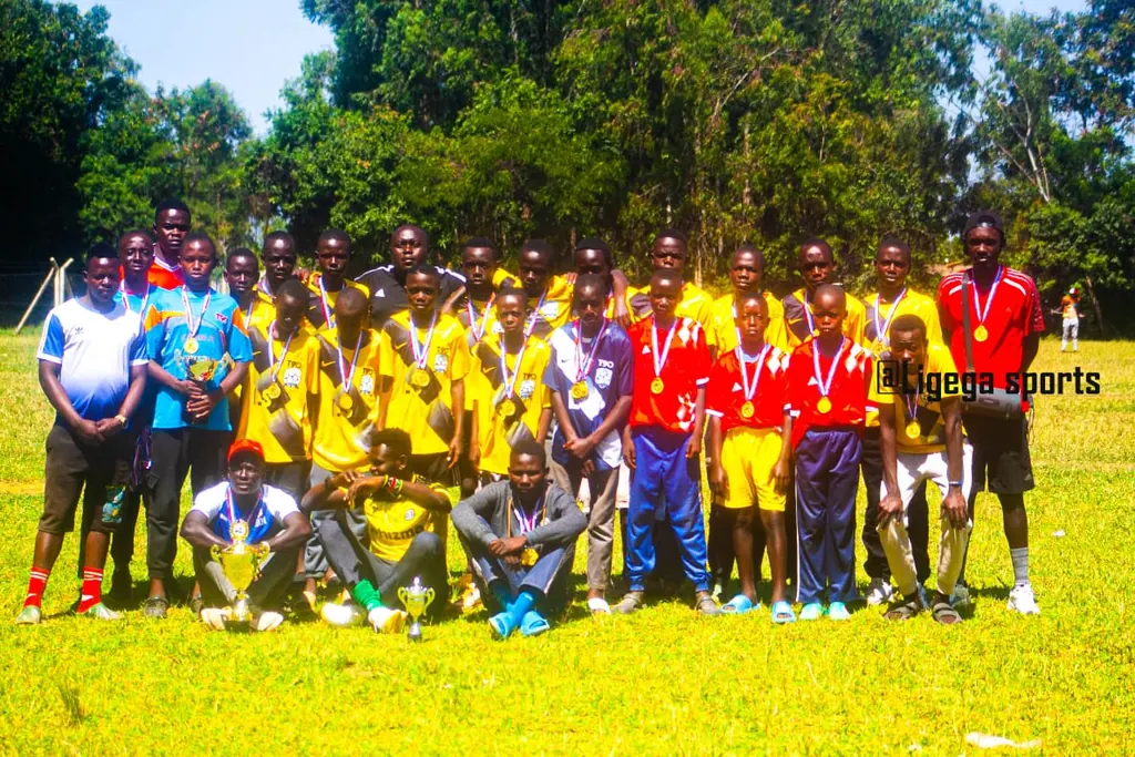 A Ligega Sports youth squad and their coaches wearing medals, with trophies set on the grass in front of them.